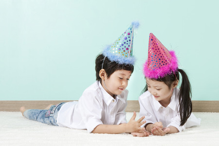 Asian cute boy and girl with party hat lying on the floor on mint backgroundの写真素材