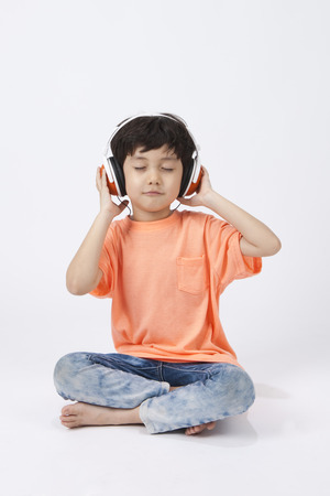 Asian cute boy listening music on floor isolated on whiteの写真素材