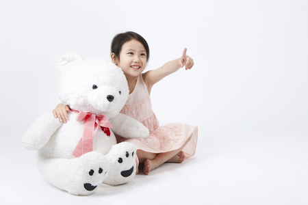 Asian cute girl pointing something with teddy bear isolated on whiteの写真素材