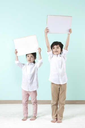 Asian cute boy and girl holding white board above their heads on mint backgroundの写真素材