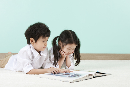 Asian cute boy and girl reading book together lying on the floorの写真素材