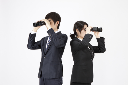 Asian business man and woman looking through a telescope isolated on whiteの写真素材