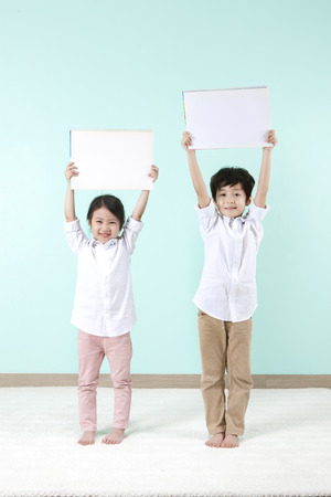 Asian cute boy and girl holding white board above their heads on mint backgroundの写真素材