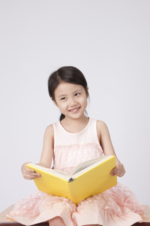 Asian cute girl reading book sitting on chair isolated on whiteの写真素材