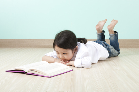 Asian cute girl reading book lying on the floorの写真素材