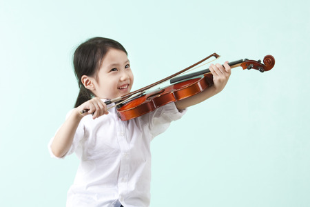 Close up Asian cute girl playing violin on chair on mint backgroundの写真素材