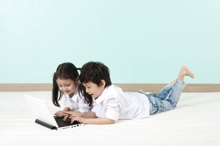 Asian cute boy and girl using laptop lying on the floorの写真素材