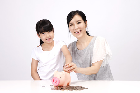 Asian mother and daughter putting money in a piggy bank isolated on whiteの写真素材