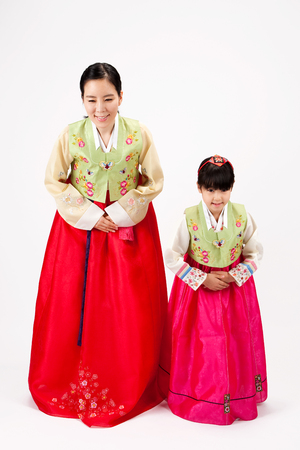 Asian mother and daughter dressed in Korean traditional clothes greeting gesture isolated on whiteの写真素材