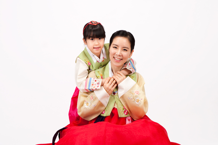 Asian mother and daughter dressed in Korean traditional clothes hug each other isolated on whiteの写真素材