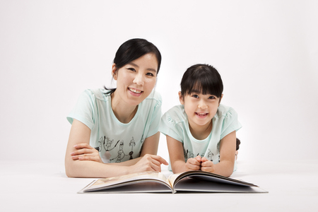 Asian mother and daughter reading book together isolated on whiteの写真素材