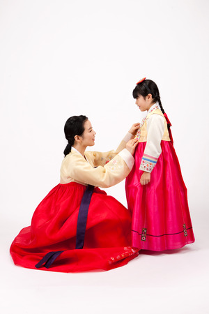Asian woman dressed in Korean traditional clothes straighten daughter's clothes isolated on whiteの写真素材