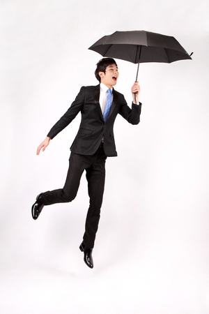 Asian business man in flying motion with umbrella isolated on whiteの写真素材