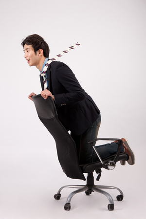 Asian young man kneeling down on the chair isolated on whiteの写真素材