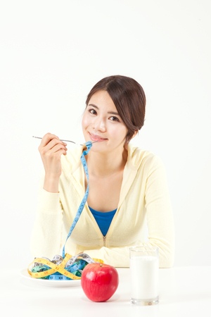 Portrait of Asian woman on diet with tape measure on plate isolated on whiteの写真素材