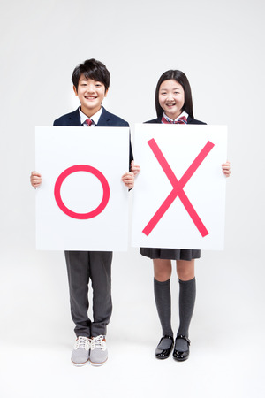 Asian middle school boy with ok sign and girl with wrong sign isolated on whiteの写真素材