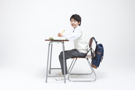 Asian middle school boy sitting on the desk to do study isolated on whiteの写真素材