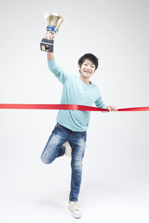 Asian teenager boy with his trophy at final line isolated on whiteの写真素材