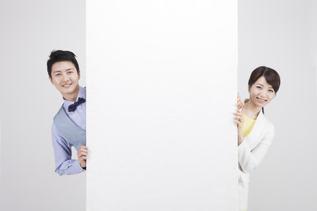 Portrait of Asian business couple hiding behind white board isolated on whiteの写真素材