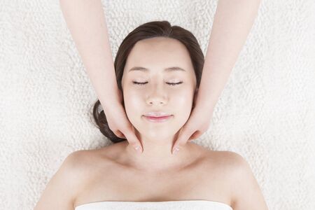 Portrait of top view Asian beautiful woman lying with closed eyes having face massage in spa isolated on whiteの写真素材