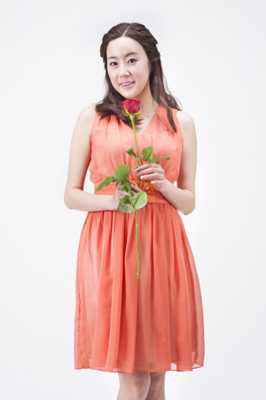 Portrait of Asian beautiful woman in dress looking happy with rose isolated on whiteの写真素材