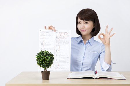 Portrait of Asian female teacher holding perfect grade test paper on the desk isolated on whiteの写真素材