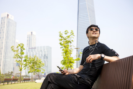 Portrait of Asian leisurely male listening music on bench outdoorの写真素材
