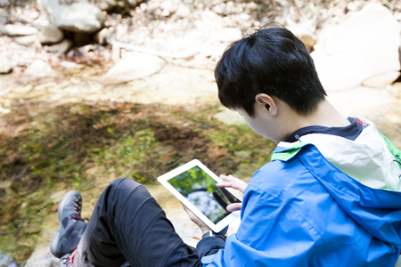 Portrait of Asian man using tablet pc next stream on mountain outdoorsの写真素材