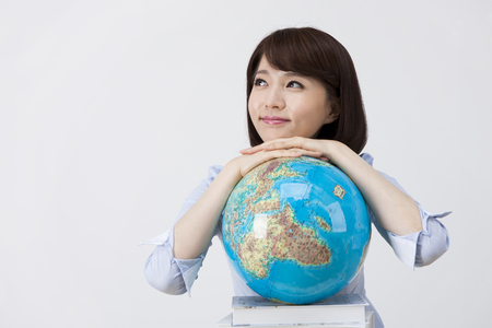 Portrait of Asian female teacher leaning on globe and pile of books on the desk isolated on whiteの写真素材
