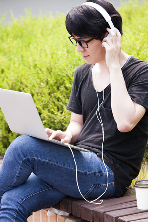 Portrait of Asian handsome man using laptop while listening music outdoorの写真素材