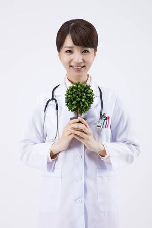 Portrait of Asian female doctor holding plant pot isolated on whiteの写真素材