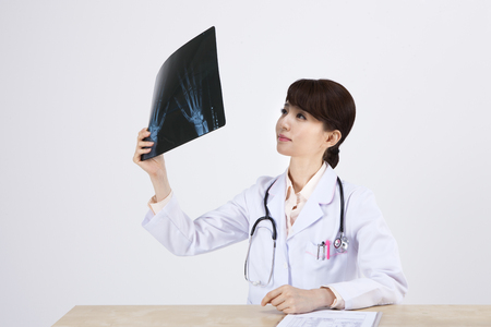 Portrait of Asian female doctor looking at x-ray films on the desk isolated on whiteの写真素材