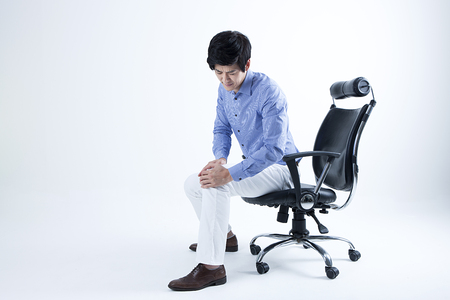 Portrait of Asian man having knee pain while sitting on the chair isolated on whiteの写真素材