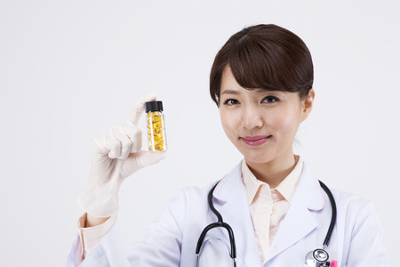 Portrait of Asian female doctor in latex gloves holing pills bottle isolated on whiteの写真素材