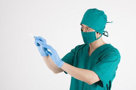 Portrait of Asian male surgeon in mask holding surgical scalpel isolated on whiteの写真素材