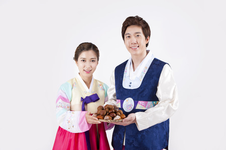 Asian happy couple in Korean traditional clothes holding chestnut basket isolated on whiteの写真素材