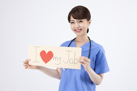 Portrait of Asian female surgeon holding board written I love my job isolated on whiteの写真素材