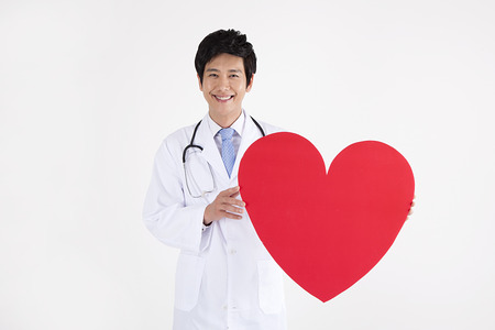 Portrait of Asian male doctor with red heart shape with smile isolated on whiteの写真素材