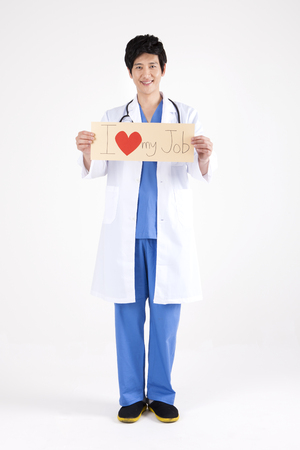Portrait of Asian handsome doctor holding board written I love my job isolated on whiteの写真素材