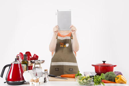 Asian housewife in apron using tablet pc to search recipe isolated on whiteの写真素材