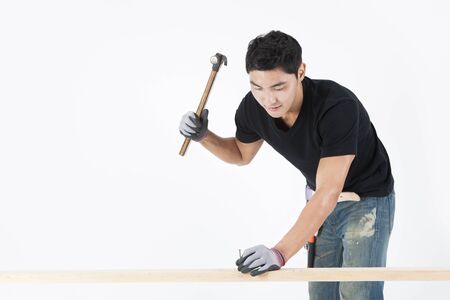 Asian handsome man in industry helmet hammering isolated on whiteの写真素材