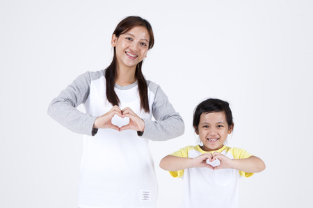 Asian multicultural family mother and daughter making heart shape with fingers isolated on whiteの写真素材