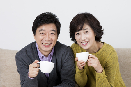 Asian middle aged couple drinking coffee on sofa bed isolated on whiteの写真素材