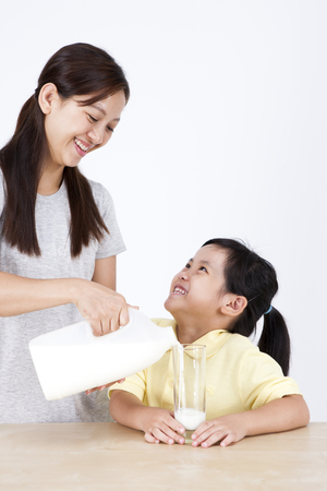 Multicultural family mother and daughter drinking milk isolated on whiteの写真素材