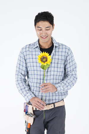 Asian handsome man with sunflower and tool isolated on whiteの写真素材