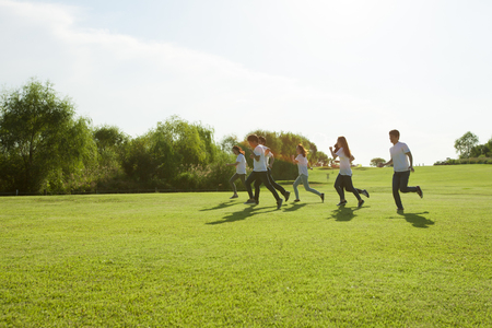 Happy Asian people group have fun run and jump with sunshine on grassの写真素材
