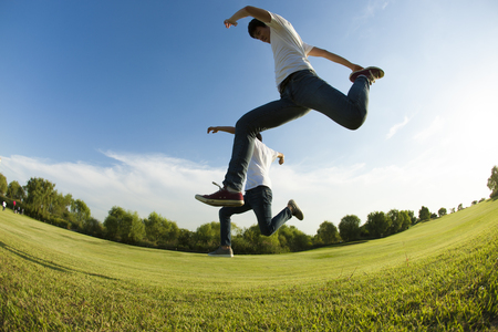 From below Happy Asian two men run and jump high on grassの写真素材