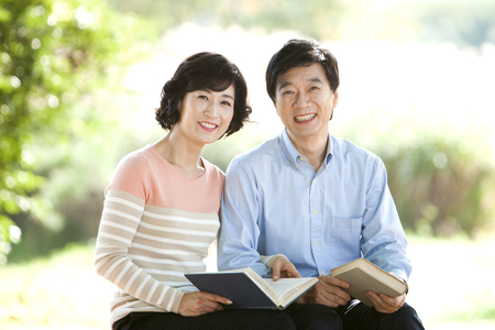Asian middle aged couple reading book outdoorの写真素材