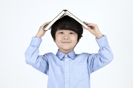 Asian cute boy with book on his head isolated on whiteの写真素材