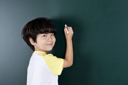 Asian cute boy writing with chalk on blackboardの写真素材